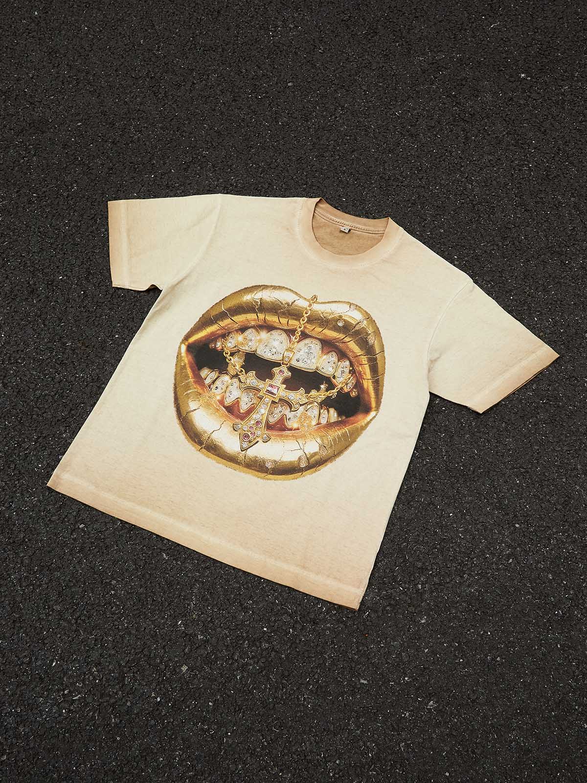 A flat lay of the Golden Cross Grillz Art Print T-shirt on a neutral grey background showing the full garment shape.