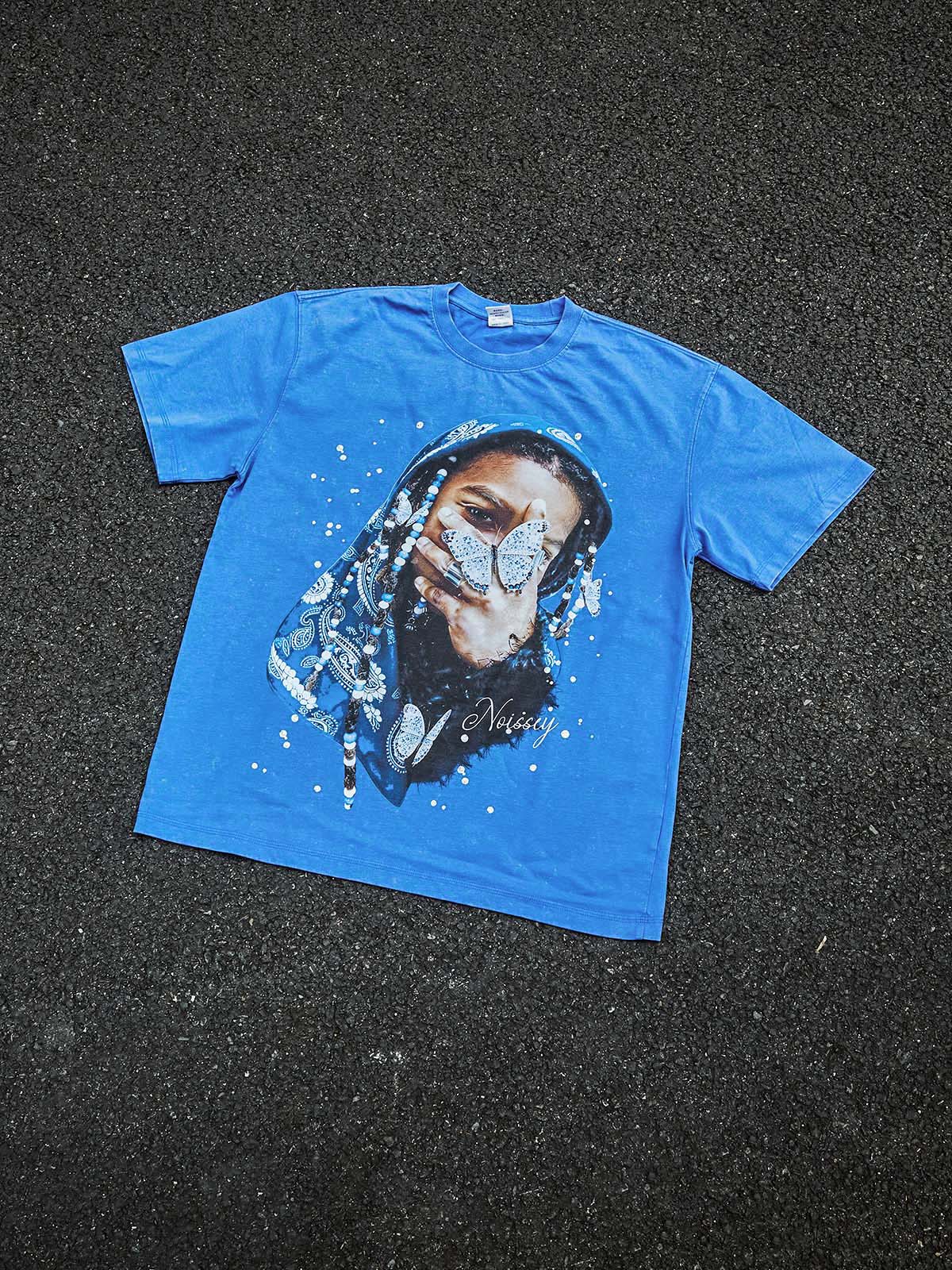 A top-down view of the indigo washed tee, highlighting the unique marbled texture of the acid-wash fabric and the centered graphic.