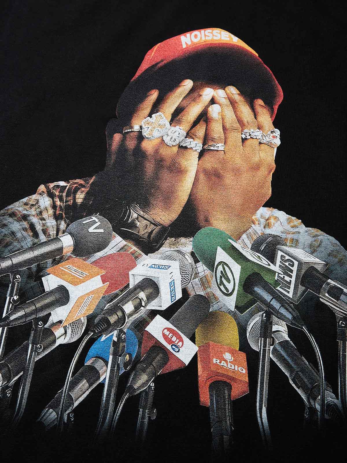 Close-up of man covering face with iced out hands surrounded by press microphones