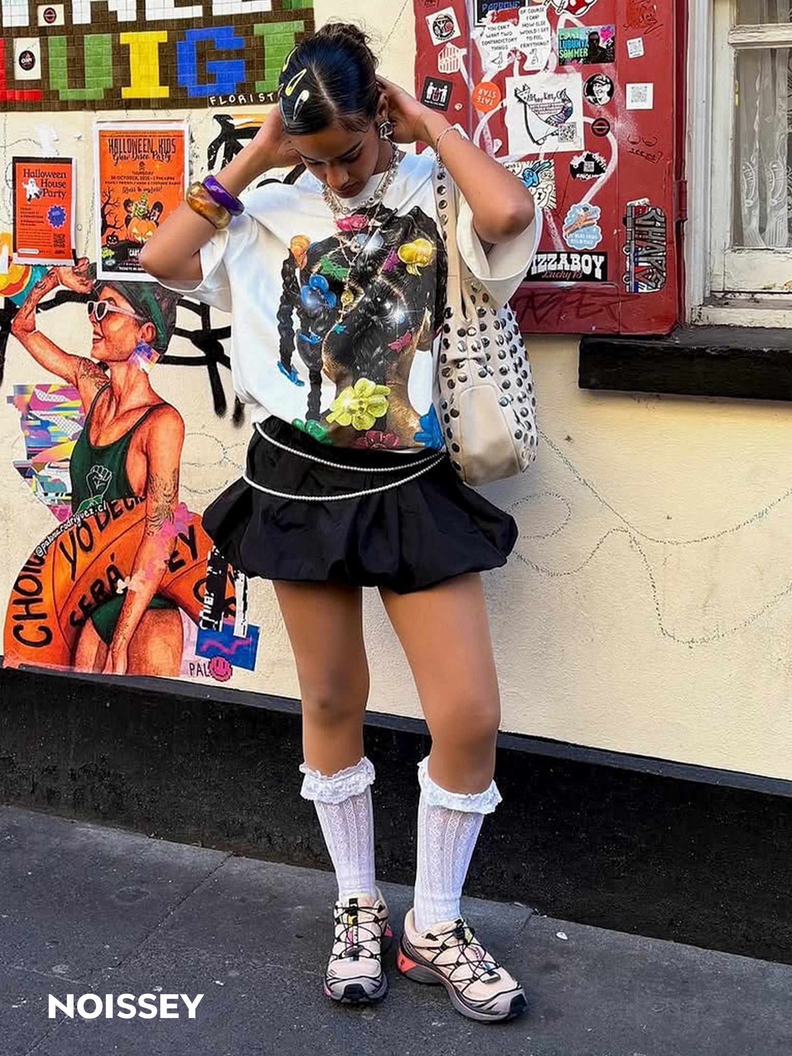 Female model wearing NOISSEY Y2K hair clip tee styled with black pleated skirt and knee high socks