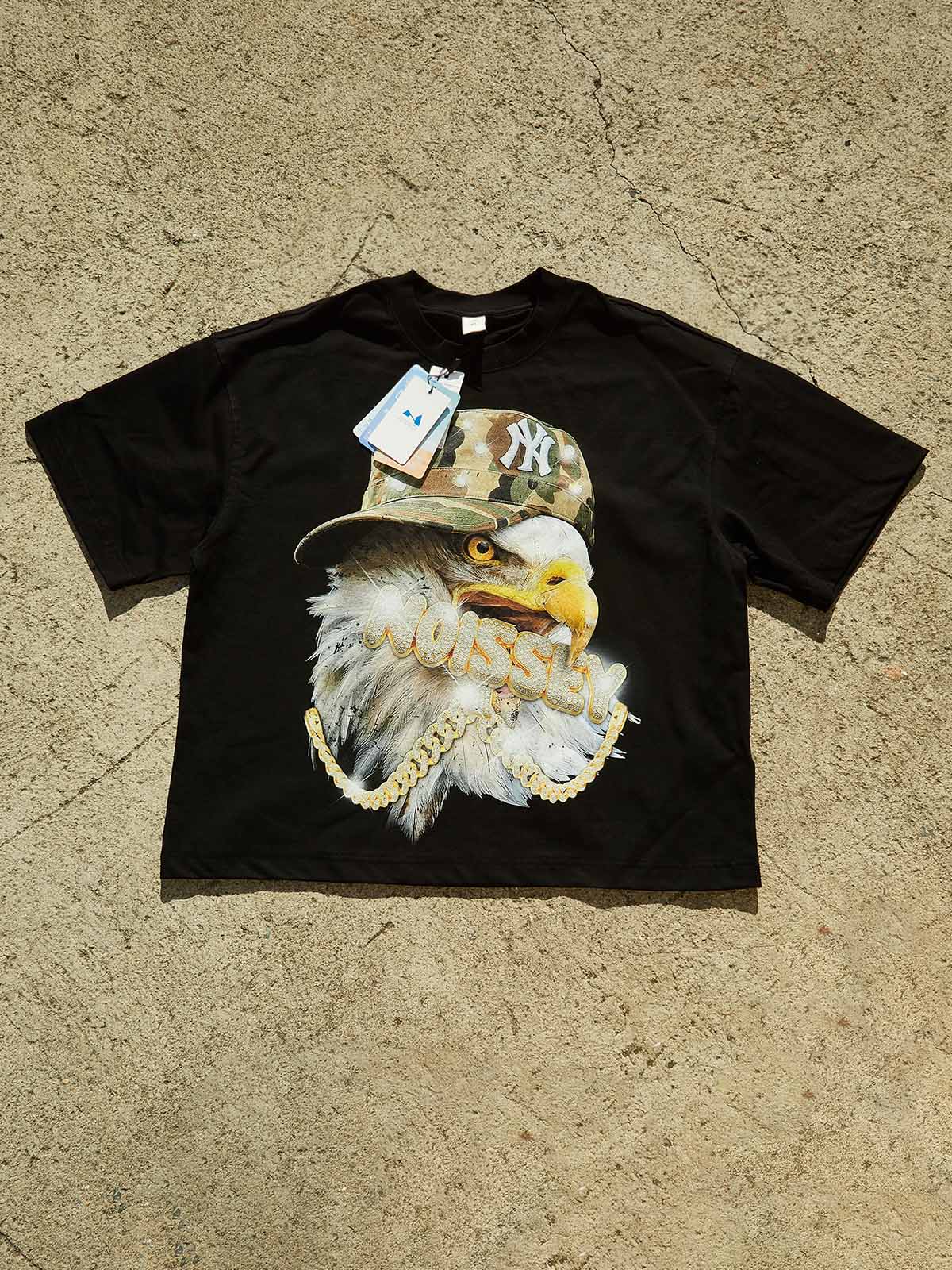 Flat lay of Noissey brand black streetwear tee with eagle and camouflage hat graphic print.