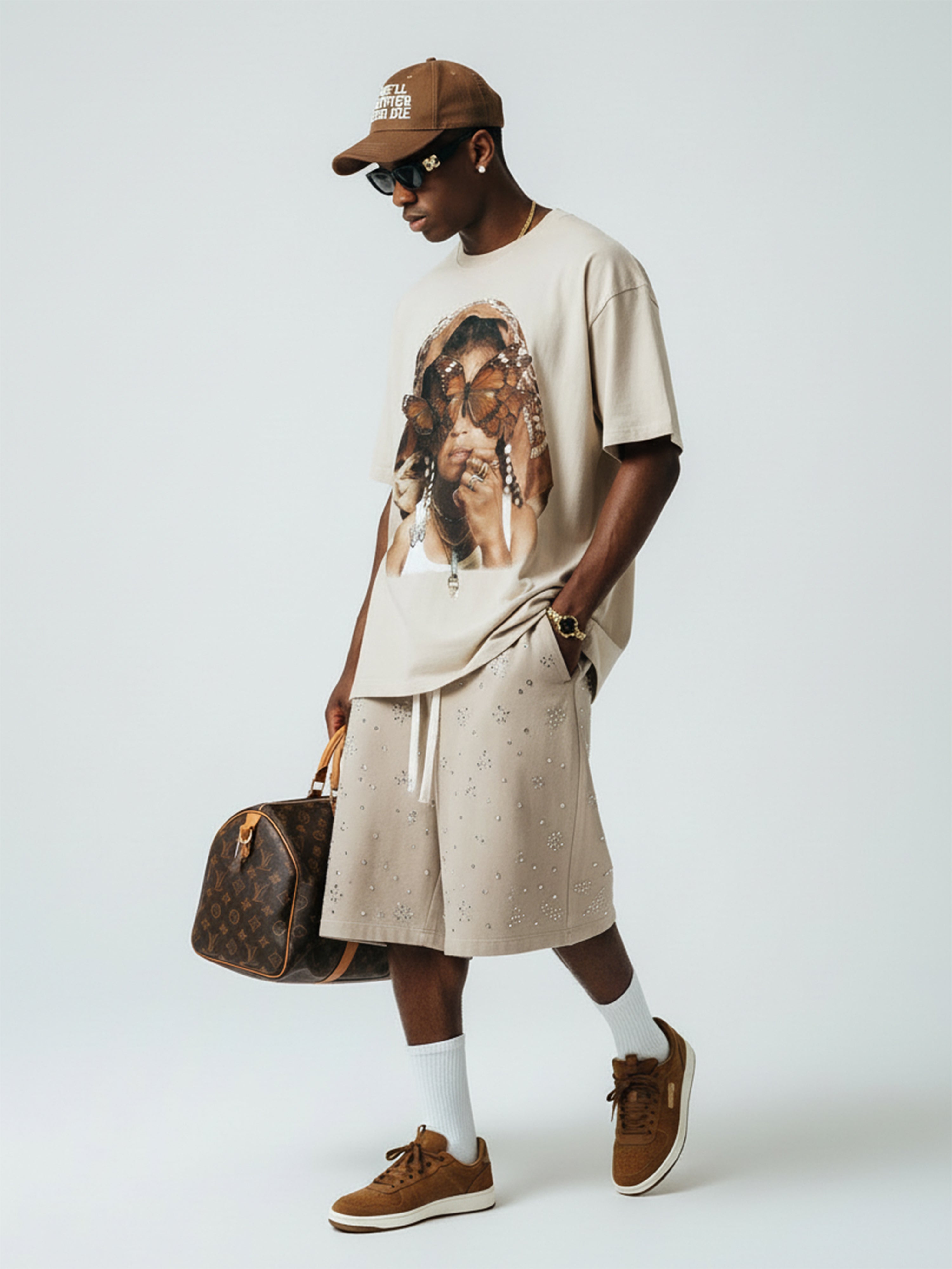 Male model wearing NOISSEY khaki butterfly tee styled with shorts and LV duffle bag